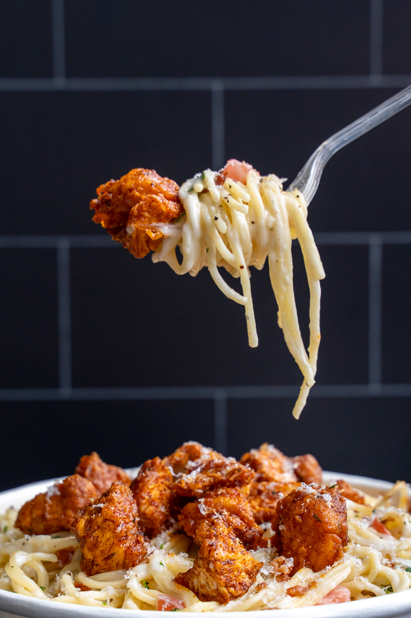 Piada hot chicken carbonara pasta with a dramatic fork pull against dark brick